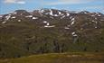 Et puklete fjellmassiv med snøklatter i flankene og en installasjon på høyeste pukkel.