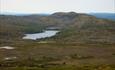 Blick über eine Ebene im Fjell mit Moor und kleinen Seen und einem Bergrücken, der sich dahinter erhebt.