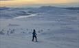 Skiløper med fantastisk skue over fjell-landskap i solnedgang.