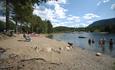 A sandy beach by a lake with people enjoying a swim and the sun.