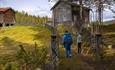 Two persons pass enter the compound of the former farm Bagnsbergatn, now a WWII memorial, towards several of the old houses.