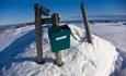 Ein Postkasten mit Tourenbuch am höchsten Punkt auf einem ausgedehnten, abgerundeten Fjellmassiv.