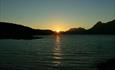 The sun is setting next to the silhouette of Mount Galdeberget at the far end of lake Bygdin.