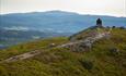 The last few steps towards the summit cairn at Jutulen with forested hillsides and a higher mountain in the background.