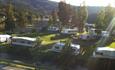 A campground by a lake during summer with caravans on a green lawn.