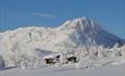 Hytte med det vinterkledde fjellet Bitihorn i bakgrunnen.