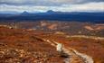 En bred sti snorer seg gjennom høstfjellet. I bakgrunnen to karakteristiske fjelltopper og vid lavfjellslandskap i mellom.