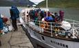 Passasjerbåt ved brygga i t fjellvann. Turfolk med ryggsekker og syklister med sykler går fra bord.