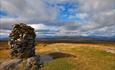 The summit cairn at Synet on a wide, open mountain plateau landscape with high massifs on the far horizon.