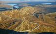 Aerial view over a road winding its way through a barren roche moutonnée landscape in the evening sun. Lakes and more mountains in the background.