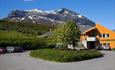 In the centre of Grindaheim with Mount Grindane in the background. It is early summer, the rowanberry trees are in bloom, and there is still snow on t