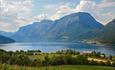 Blumenwiese und grüne Weiden in Vang, im Hang oberhalb von Grindaheim mit Aussicht über den See Vangsmjøse. Das Skutshorn dominiert den HIntergrund am anderen Seeufer.