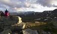 En person sitter på en stor stein og ser ut over fjellandskap i motlys