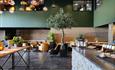 Restaurant interiour with slate floor, stone bar counter, a warm wooden panel on the wall with green shielding and many warm yellow hanging lamps. An