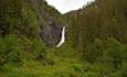 The waterfall Juvfossen falls over a rocky cliff surrounded by lush green vegetation.