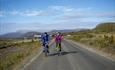 Two cyclists in colourful jackets cycling across the open mountainous landscape of the mountain farming area Stølsvidda along the Mjølkevegen cycling