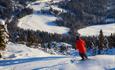 Skier in a red jacket at Stavadalen Skisenter with a view downhill to the bottom of the slope.