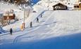 Children's area at Stavadalen with a button lift, a broad slope and some slalom sticks and arch to exercise swings.