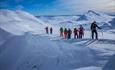 Group of 9 persons on their way up a mountain on randonee skis. Snow covered mountains in the background.