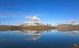 View over Lake Tyin with its calm water surface reflecting high pointed peaks in the background.