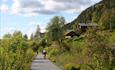 A family cycles along Valdresbanevegen, past blooming trees and meadows.