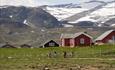 Cyclists in fron of red farm houses with a dramatic mountain scenery in the background.