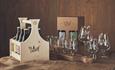 A wooden box with beer bottles and a number of beer glasses arranged on a hemp cloth.