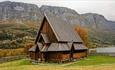 Øye Stavkirke med høstfarger på trærne i bakgrunnen.