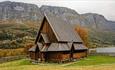 Øye Stavkirke med høstfarger på trærne i bakgrunnen.