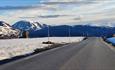 Bergstraße mit schneebedeckten Bergen im Hintergrund.