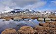 snødekte fjell speiler seg i blikkstille fjellvann