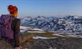 Women up close seen from behind while enjoying view towards snow patched mountains.