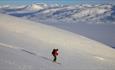 Person på vei ned fjellside med randoneeski, vid utsikt over snødekt fjellandskap