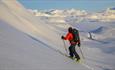 Person på vei opp fjellside med randoneeski, vid utsikt over snødekt fjellandskap