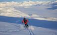 Person på vei ned fjell med randoneeski, vid utsikt over snødekt fjellandskap