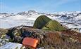 Grønt fjelltelt på en bar rabb med fjellet Bitihorn i bakgrunnen. Det ligger mye snø i terrenget enda.