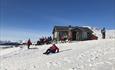 A serviced warming hut along a skiing track with people enjoying the sun and the snow.