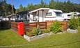 Permanent caravans with wooden deck and outdoor furniture, white fence and green lawn.