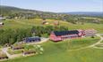 Dronenfoto eines roten Holzhotels in einer grünen Wiesenlandschaft