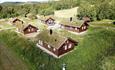 6 traditional wooden cabins with grass roof surrounded by lush birch forest and meadow.