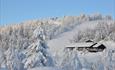 Gamlestølen Fjellstue med skibakken og snødekte trær i bakgrunnen.