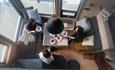 Image taken from above showing three persons around a table in a small living room with large windows