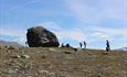 Small personens next to a large boulder.