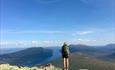 A hiker on a viewpoint with view over a long lake surrounded by mountains.