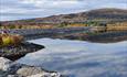 On a dam with the lake lying mirror-calm. In the background an autumn-coloured hill.