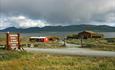 Die Haugseter Fjellstue mit Grasdach am Ufer des Sees Vinstre. Im Hintergrund Berge und dunkle Wolken am Himmel.