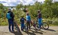 A family of four on bicycles watches a grazing cow.