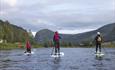 Three stand-up boarders on a calm river with a forested hill in the background