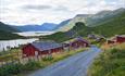 A farm road leads to the idyllic mountain farm area of Strø, with lakes and mountains in the background.