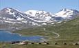 En fjellstue og et knippe hytter ved et vann i storslått høyfjellslandskap